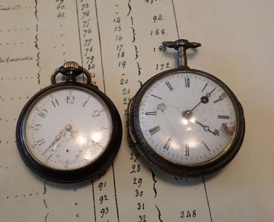 deux vieilles montres de poche posées sur un morceau de papier
