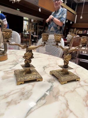two brass candles on a marble table with a woman in the background