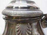 une théière en argent avec son couvercle, posée sur une table