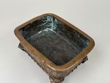 a small bronze bowl on a stand on a white surface