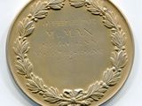 une médaille d'or ornée d'une couronne, posée sur un fond blanc