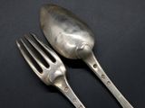 two silver spoons and a fork on a black surface