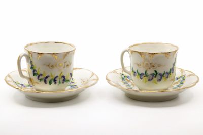 two cups and saucers with floral designs on them on a white surface