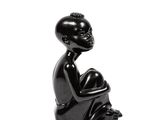 sculpture noire représentant une femme assise à genoux sur un fond blanc