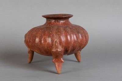 un petit vase rouge posé sur un socle, sur une surface grise