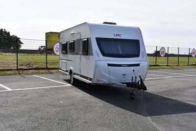 un camping-car blanc garé sur un parking près d'une clôture