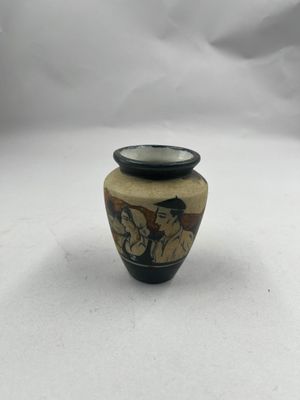 un petit vase orné d'une peinture, posé sur une surface blanche