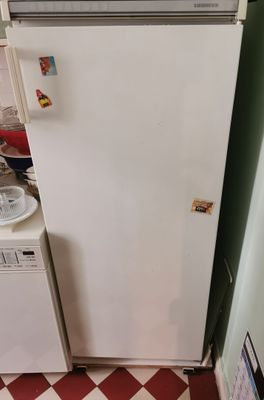un réfrigérateur blanc dans une petite cuisine au sol à carreaux rouges et blancs