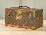 Une malle Louis Vuitton posée sur une table en bois, sur fond vert