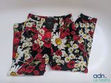 Le pantalon est noir, orné de fleurs blanches et rouges.