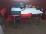 une table blanche avec des chaises rouges et une pile de papiers posée dessus