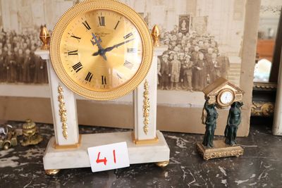 une horloge en or posée sur une table en marbre, à côté d'une petite figurine