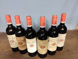 six bottles of red wine are lined up on a wooden table