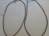deux colliers en cuir noir avec des fermoirs en argent, posés sur une surface blanche