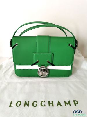 a green longchamp purse sitting on top of a white cloth