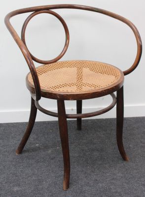 une photo d'une chaise en bois avec une assise tressée, posée sur un sol recouvert de moquette