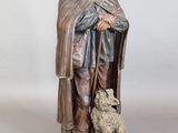 statue représentant un homme coiffé d'un chapeau et vêtu d'une cape, tenant un chien dans ses bras