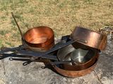 des casseroles et des poêles posées sur une dalle de pierre dans l'herbe