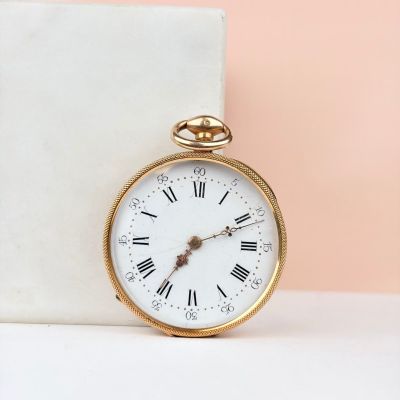 montre de poche en or avec des chiffres romains, posée sur un bloc de marbre
