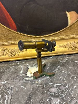 un télescope ancien en laiton posé sur une table en marbre, avec un tableau en arrière-plan