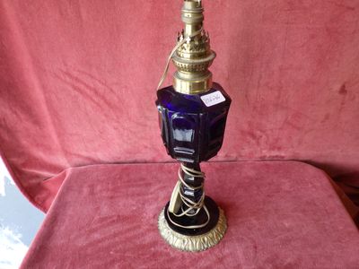 a blue glass vase with a gold base on a pink cloth
