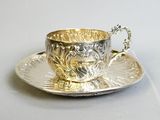 a silver cup and saucer sitting on a silver plate