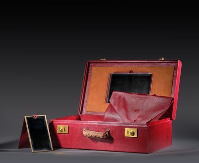 une valise rouge contenant un miroir, posée sur une surface grise