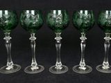 six green wine glasses lined up in a row on a black background