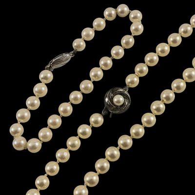un collier de perles blanches muni d'un fermoir en argent, sur fond noir