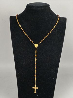un collier chapelet en or orné d'une croix, posé sur un mannequin noir