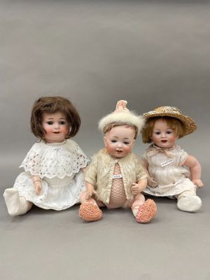 trois poupées en porcelaine assises les unes à côté des autres sur une surface grise