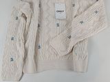 Le pull est blanc et est orné de boutons bleus.