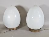 une paire de lampes blanches en forme d'œuf avec des pieds en laiton, sur fond blanc
