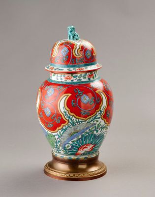 une image représentant un vase rouge et bleu muni d'un couvercle, posé sur un socle
