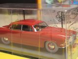 a red toy car in a clear box on a yellow table