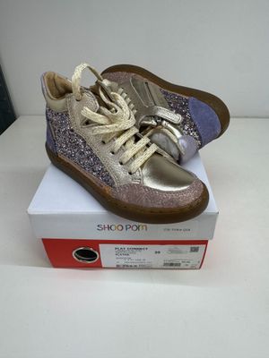 des baskets argentées et violettes pailletées posées sur une boîte blanche