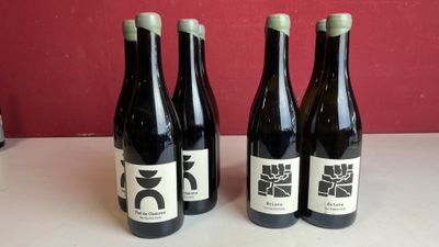 Trois bouteilles de vin sont posées sur une table, avec un mur rouge en arrière-plan.