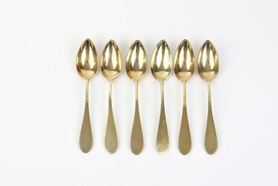 five gold spoons are lined up in a row on a white surface