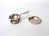 a small metal strainer with a spoon next to it