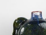 a blue vase with a green handle on a white surface