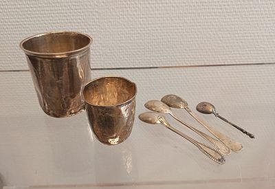 une coupe en argent, des cuillères et un repose-cuillères posés sur une table en verre