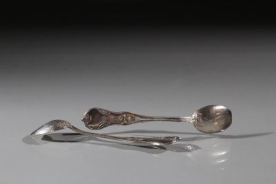 deux cuillères en argent et un repose-cuillère posés sur une surface blanche