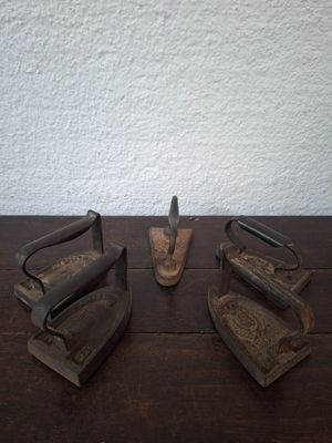 three old irons sitting on a table with a white wall in the background