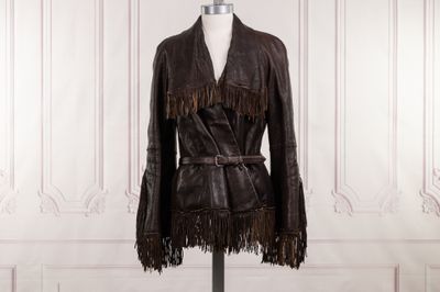 une veste en cuir à franges posée sur un mannequin devant un mur blanc