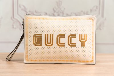 la pochette Gucci blanche et dorée, sur laquelle est imprimé le mot « Gucci »
