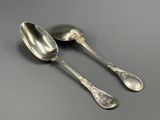 two silver spoons sitting on top of a table next to each other