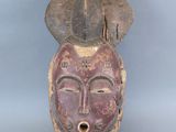 une image représentant un masque en bois orné d'un visage et d'un chapeau
