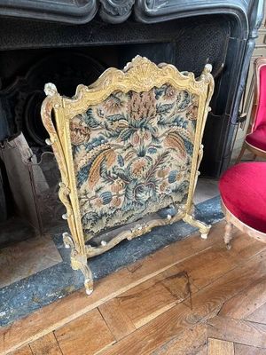 un fauteuil rouge placé devant une cheminée ornée d'une tapisserie