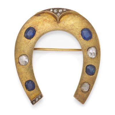 a close up of a gold horseshoe broochle with blue and white stones