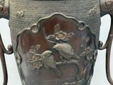 a large metal vase with a bird and flowers on it